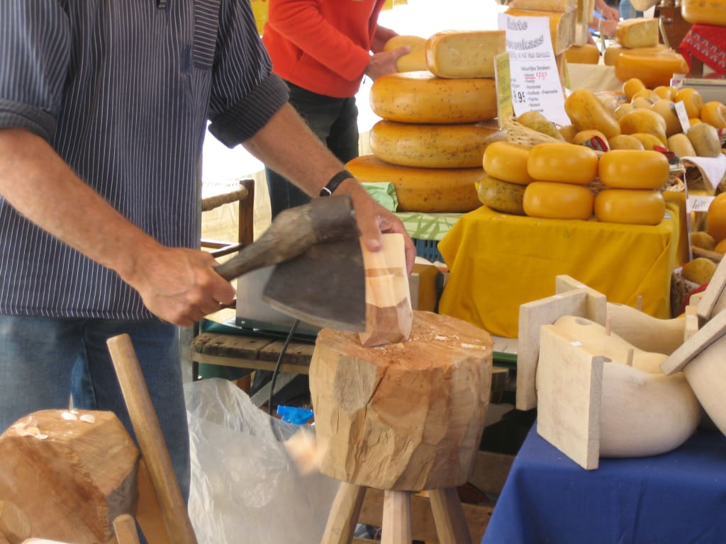 Artigiano al lavoro in un mercato tradizionale del formaggio nei Paesi Bassi, con grandi forme di Gouda esposte.